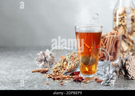 Weihnachtlicher Kräutertee mit Zimt, Anis und getrockneten Kräutern. Kräutertee mit Gewürzen auf grauem Hintergrund. Stockfoto