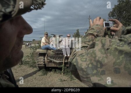 Besucher der Nachstellung von Krieg und Frieden sitzen auf Tank und machen Fotos Stockfoto