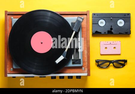 Retro-Stil, 80er Jahre, Pop-Kultur Attribute auf einem gelben Hintergrund. Vinyl-Player, 3D-Brille, Audio, Videokassette. Draufsicht Stockfoto