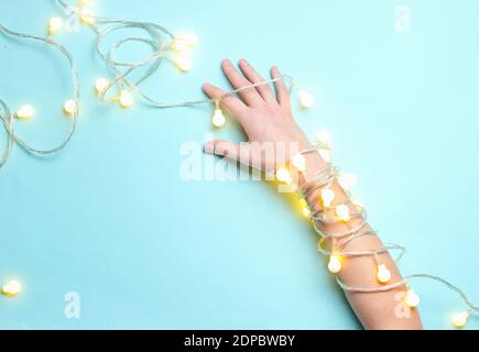 Minimalismus-Trend. Weibliche Hand mit hellen leuchtenden Girlanden von Glühbirnen auf blauem Hintergrund gewickelt. Draufsicht Stockfoto