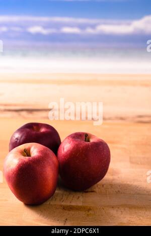 3 rote Äpfel liegen auf einem Holztisch in der Nähe des Am Meer Stockfoto
