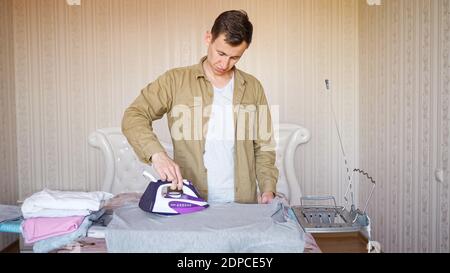 Der junge Mann bügelt zum ersten Mal auf einem Bügelbrett. Stockfoto