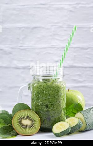 Grüner Detox Smoothie im Glas mit Gurke, Apfel, Kiwi und Spinat auf weißem Hintergrund. Vertikales Format. Gesunde Ernährung und Getränke Konzept. Stockfoto