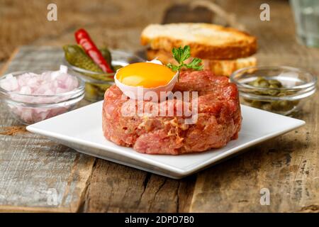 Steak Tartare mit offenem Ei auf Holz Stockfoto