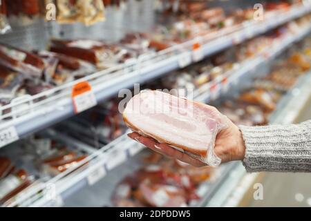 Die Hand des Kunden hält ein geräuchertes Schweinefleisch im Supermarkt Stockfoto