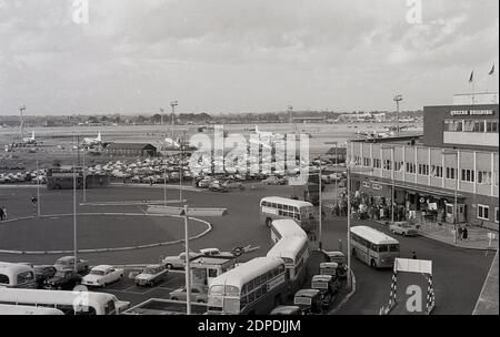 Ende der 1950er Jahre, historischer London Airport, Außenansicht des Startbahnbereichs mit Propellerflugzeugen und des zentralen Bereichs mit geparkten Autos, Bussen und Taxis, die vor dem Queens Building warten, wo sich die Flughafenverwaltung befindet. Der Flughafen wurde später in London Heathrow umbenannt. Flughafen. Das von Frederick Gibberd entworfene Queen's Building wurde 1955 offiziell von Königin Elizabeth II. Eröffnet und obwohl Büros für BAA waren, wurde das Gebäude zu einer beliebten Attraktion für Besucher, da es Aussichtsplattformen über dem Flughafen und Dachgärten hatte. Sie wurde 2009 abgerissen. Stockfoto