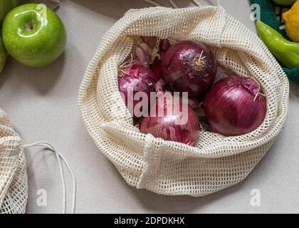 Von oben gesehen ein Netz Öko-Beutel mit vier lila Zwiebeln innen. Einige nachhaltige Äpfel und Paprika rundherum runden die Szene ab. Stockfoto