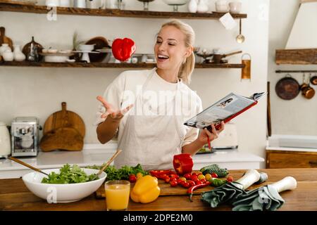 Schöne aufgeregt Frau Kochbuch lesen und drehen Paprika, während Mittagessen in der Küche Stockfoto