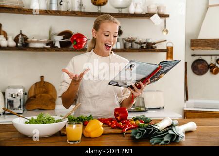 Schöne aufgeregt Frau Kochbuch lesen und drehen Paprika, während Mittagessen in der Küche Stockfoto