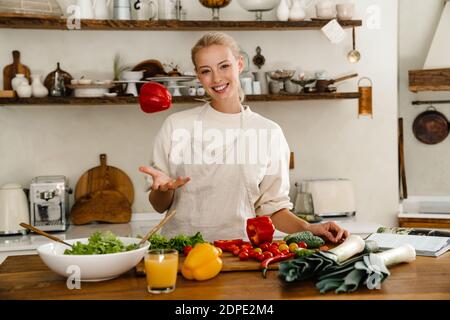 Schöne glückliche Frau lächelt und dreht Paprika während der Herstellung Mittagessen in gemütlicher Küche Stockfoto