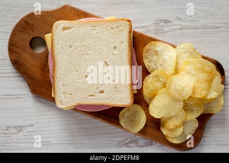 Hausgemachtes Bologna und Käse-Sandwich auf einem rustikalen Holzbrett auf einem weißen Holztisch, Blick von oben. Flach liegend, Draufsicht, von oben. Stockfoto