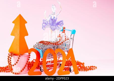 Roter Weihnachtsbaum und die Inschrift 2021 im Warenkorb. Weihnachtsbaumschmuck im Warenkorb auf rosa Hintergrund. Urlaubskonzept Stockfoto