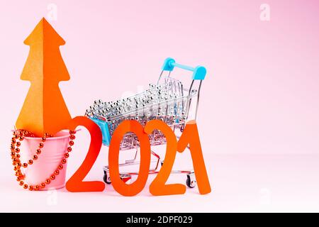 Roter Weihnachtsbaum und die Inschrift 2021 im Warenkorb. Weihnachtsbaumschmuck im Warenkorb auf rosa Hintergrund. Urlaubskonzept Stockfoto
