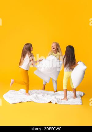 Nette kleine Mädchen kämpfen mit Kissen auf farbigem Hintergrund Stockfoto