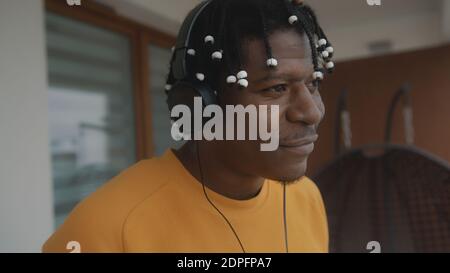 Porträt eines afroamerikanischen schwarzen Mannes mit Dreadlocks, der die Musik auf dem Balkon mit dem Headset hört. Hochwertige Fotos Stockfoto