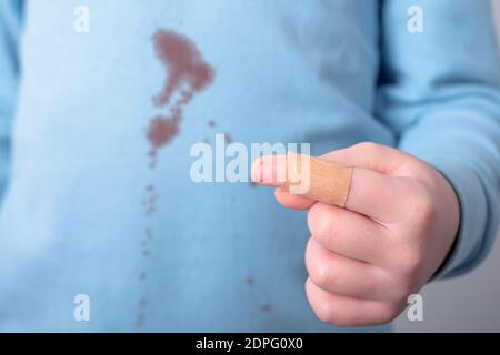 Nahaufnahme von Kind Finger mit Kleben-Gips. Schmutzige Blutfleck auf T-Shirt auf dem Hintergrund. Platz für Text Stockfoto