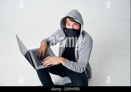 Ein Mann in einer Maske sitzt auf dem Boden innen Vor einem Laptop-Computer Hacking Verbrechen Stockfoto