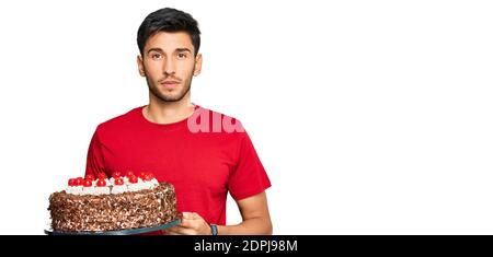 Junger schöner Mann feiert Geburtstag mit Kuchen Denken Haltung und Nüchterner Ausdruck, der selbstbewusst aussieht Stockfoto