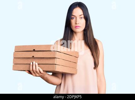Junge schöne kaukasische Frau hält Lieferung Pizza Box Denken Haltung Und nüchterner Ausdruck, der selbstbewusst aussieht Stockfoto