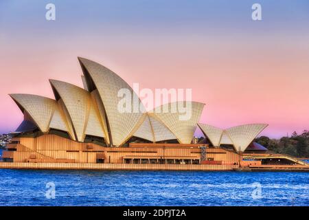 Sydney, Australien - 11. August 2020: Sydney Opera House Seitenansicht am Ufer des Hafens von Sydney bei Sonnenuntergang unter rosa Himmel. Stockfoto