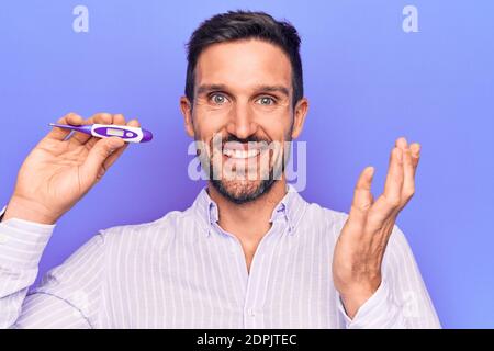 Junger schöner Mann Kontrolle Temperatur halten Thermometer über lila Hintergrund Erfolge mit glücklichen Lächeln und Siegerausdruck feiern Stockfoto