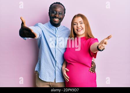 Junge interracial Paar erwartet ein Baby, berühren schwangeren Bauch lächelnd freundlich bietet Handschlag als Gruß und einladend. Erfolgreiches Geschäft. Stockfoto