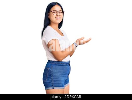 Junge schöne asiatische Mädchen tragen lässige Kleidung und Gläser beiseite zeigen mit Händen offenen Handflächen zeigen Kopieplatz, präsentiert Werbung Smilie Stockfoto