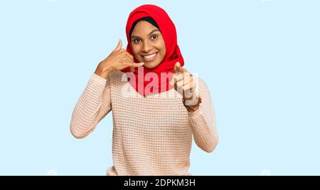 Junge afroamerikanische Frau trägt traditionelle islamische Hijab Schal lächelnd dabei, auf der Telefongeste zu sprechen und auf Sie zu zeigen. Rufen Sie mich an. Stockfoto