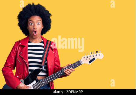 Junge afroamerikanische Frau spielt E-Gitarre erschrocken und erstaunt mit offenem Mund für Überraschung, Unglauben Gesicht Stockfoto