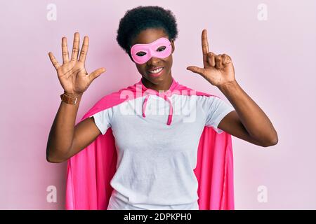 Junge afroamerikanische Mädchen trägt Superhelden Maske und Cape Kostüm Zeigen und zeigen mit den Fingern Nummer sieben beim Lächeln Selbstbewusst und happ Stockfoto