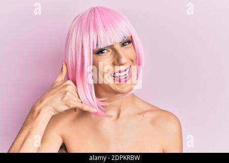 Junger Mann trägt Frau Make-up trägt rosa Perücke lächelnd tun Telefon Geste mit Hand und Fingern wie am Telefon sprechen. Kommunikation concep Stockfoto