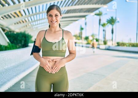 Junge blonde Sportlerin trägt Sportkleidung mit Händen auf dem Bauch in der Stadt. Stockfoto