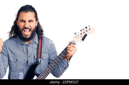 Junger arabischer Mann spielt E-Gitarre schreiend stolz, feiert Sieg und Erfolg sehr aufgeregt mit erhobenen Armen Stockfoto