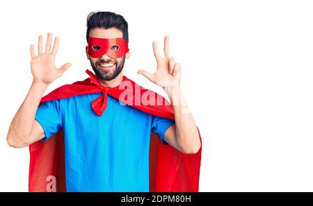 Junger schöner Mann mit Bart trägt Superhelden Kostüm zeigt und zeigt mit den Fingern Nummer acht, während lächelnd zuversichtlich und glücklich. Stockfoto