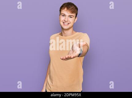Junge kaukasische Mann in legerer Kleidung lächelnd fröhlich bietet Handfläche Hand geben Hilfe und Akzeptanz. Stockfoto