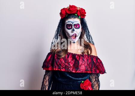 Junge Frau trägt Tag der Toten Kostüm über weiß im Schockgesicht, skeptisch und sarkastisch, überrascht mit offenem Mund Stockfoto