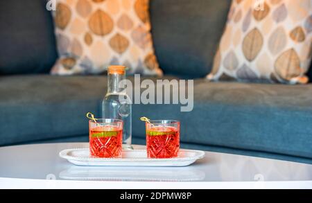 Nahaufnahme von zwei Campari-Gläsern auf weißer Tischfläche In Lounge-Interieur verschwommen Hintergrund mit grauen Sofa und Herbst Kissen Stockfoto