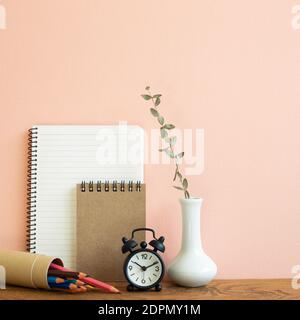 Notizbuch, Uhr, Bleistifte mit Vase aus Eukalyptus auf Holztisch. Rosa Hintergrund. Arbeits- und Studienort Stockfoto