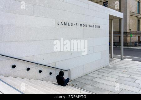 Mann mit EINER Kapuze sitzt auf der Treppe an der James Simon Galerie In Berlin Stockfoto