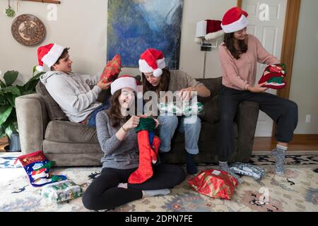 Vier Geschwister im College-Alter mit Weihnachtsmützen öffnen weihnachtsgeschenke Stockfoto