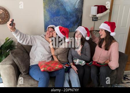 Vier Geschwister im College-Alter, die Weihnachtsmützen tragen, posieren für ein Selfie Stockfoto