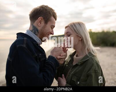 Seitenansicht des hübschen jungen Mannes mit Tätowierung und hübsch Blonde Frau lächelt und beleuchtet Marihuana Joint während des Stehens Verschwommener Hintergrund des Herbstes Stockfoto