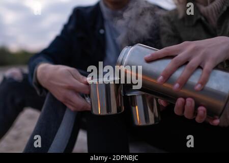 Nahaufnahme anonyme weibliche Füllung Tassen mit frischem heißen Tee für Freund beim Entspannen in der Natur am Abend Stockfoto