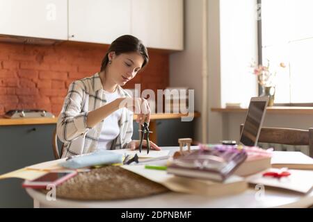 Junge Frau mit Trennwerkzeug beim Zeichnen Entwurf für Hochschule Aufgabe sitzen am Tisch in der Küche Stockfoto