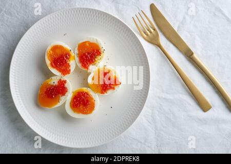 Weich gekochte Eier, geschält und in zwei Hälften geschnitten, und Lachskaviar auf weißem Teller liegen. Stockfoto