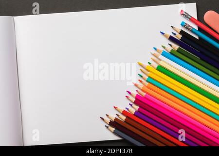 Buntstifte und Skizzenbuch auf dunklem Hintergrund mit Kopierfläche, Draufsicht. Stockfoto