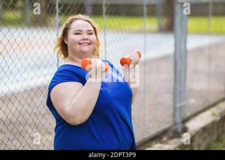 Eine junge Blondine von plus size macht Übungen mit Hanteln auf der Straße. Gesundes Lifestyle-Konzept. Stockfoto