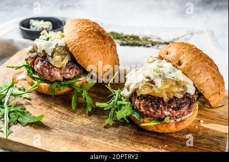 Leckere Burger mit Blauschimmelkäse, marmorierten Rindfleisch, Zwiebelmarmelade und Rucola. Grauer Hintergrund. Draufsicht. Stockfoto