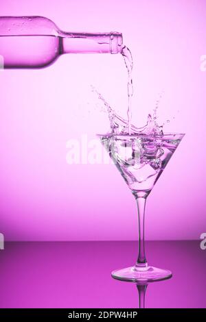 Rosa Flasche verschüttet Flüssigkeit in ein Cocktailglas und macht Splash. Rosa Hintergrund, alkoholische Getränke und Cocktails Konzept. Stockfoto