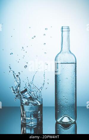 Flasche Eiswasser mit Tropfen, und Glas Wasser mit Eis fallen mit Spritzer. Wasserspritzer und erfrischende Getränke Konzept. Stockfoto